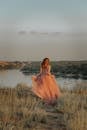 Woman in Brown Dress Sitting on Grass Field Near Lake