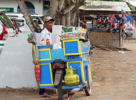 Street vendor beside a colorful mobile food cart on a bustling urban street, selling snacks.