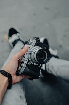 A close-up of a vintage camera being held by a casually dressed person, emphasizing retro photography.