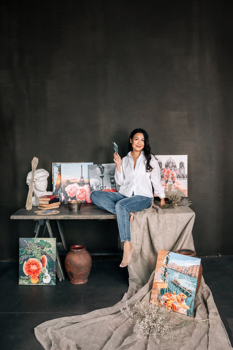 Woman Sitting In An Art Studio Among Her Paintings 