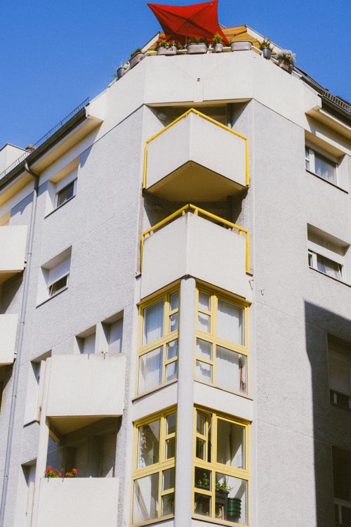 Free Low-angle view of a white apartment building with yellow balconies under clear blue sky. Stock Photo