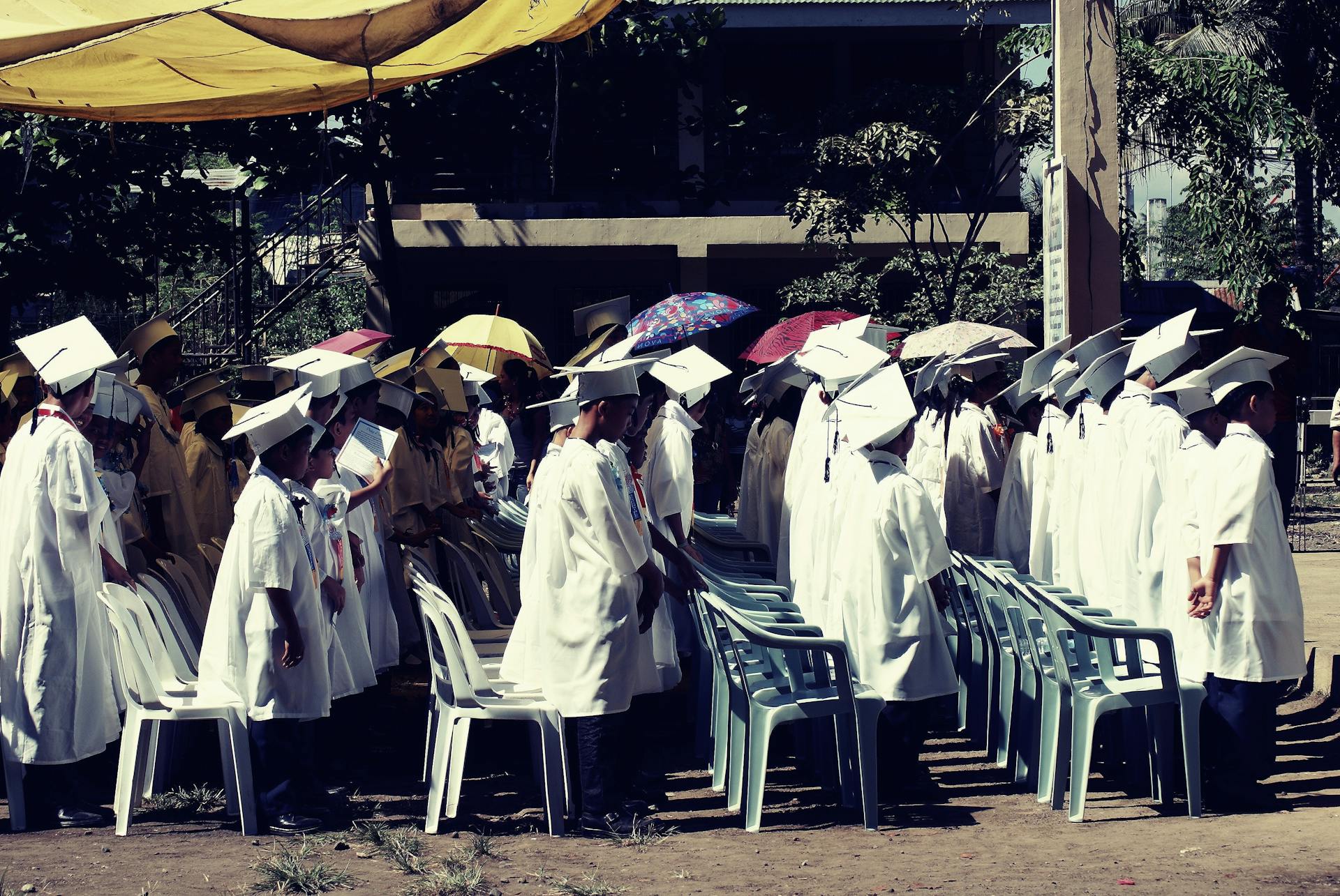 Group of children in academic gowns celebrating graduation outdoors.