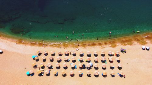 Free Aerial view of a sunny beach in Greece with umbrellas and swimmers enjoying the sea. Stock Photo