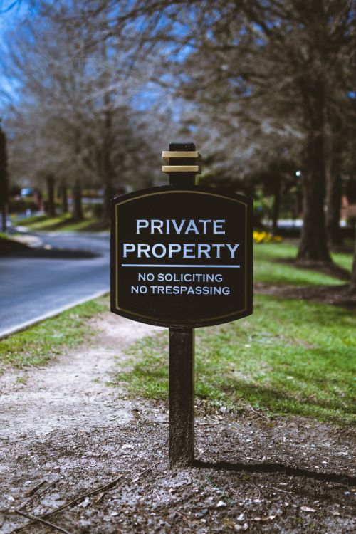 Free Black sign displaying 'Private Property' warning with trees in the background. Stock Photo