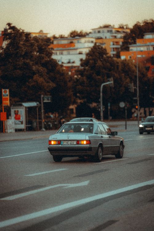 Free A classic sedan navigates a bustling city street at dusk, surrounded by trees and buildings. Stock Photo