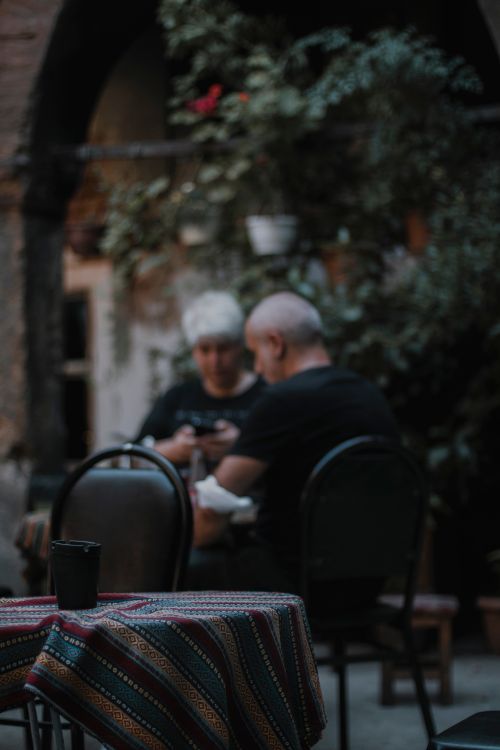 Free Elderly couple enjoying time together at an outdoor café surrounded by greenery. Stock Photo