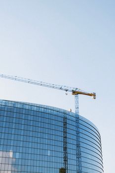 Modern glass building facade with a construction crane under a clear sky. Perfect for architecture themes.