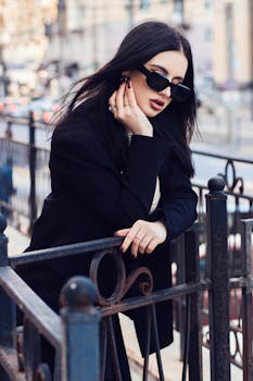 Stylish woman with black hair and sunglasses striking a pose on a city street during the day.