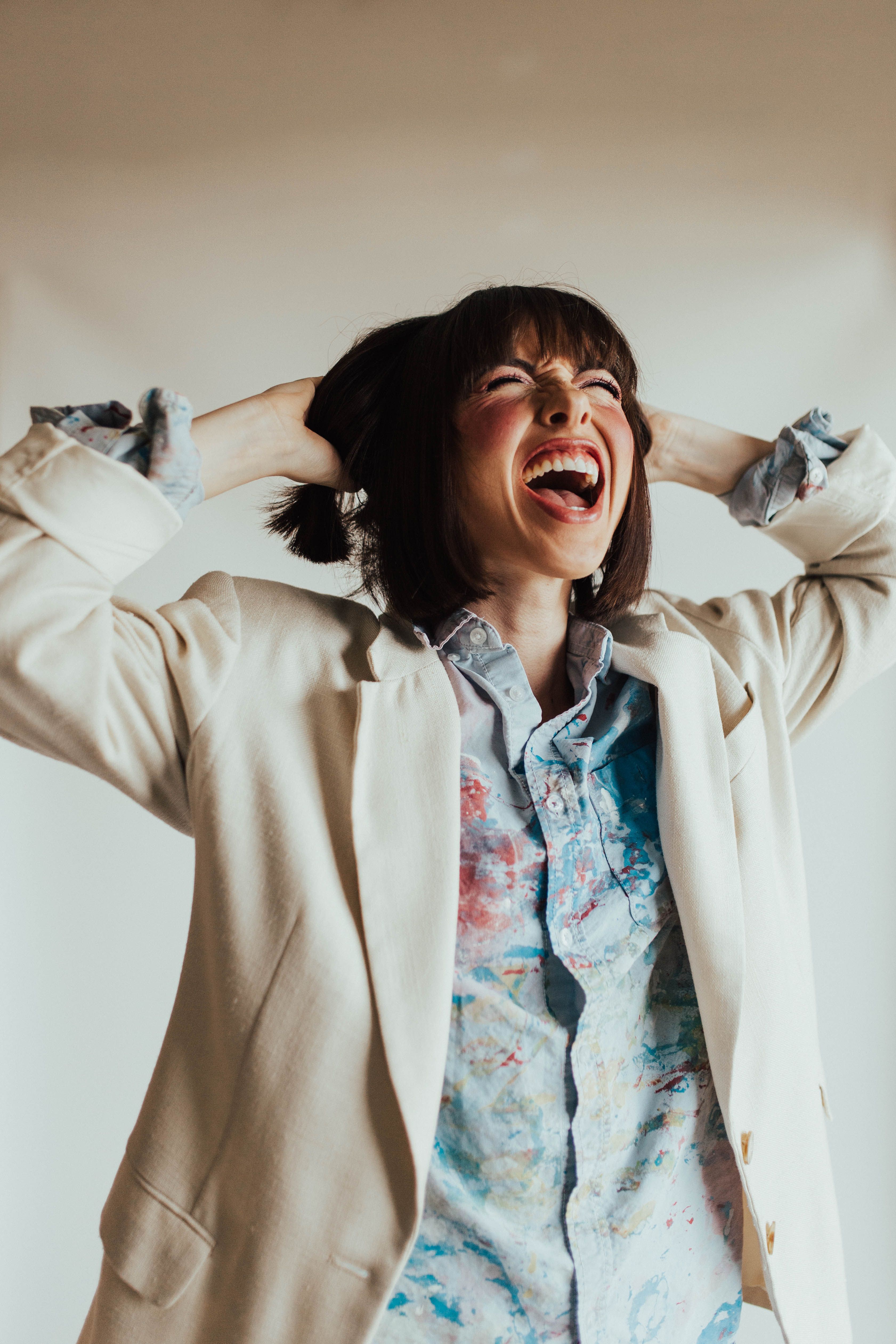 A joyful woman with short hair and a beige blazer displays excitement and energy.