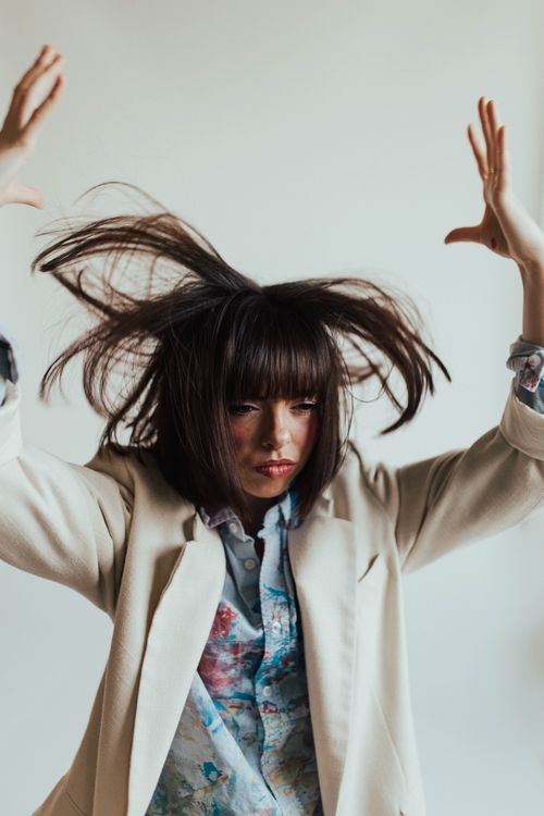 Free Portrait of a woman with messy hair in motion, wearing a beige suit and colorful shirt. Stock Photo