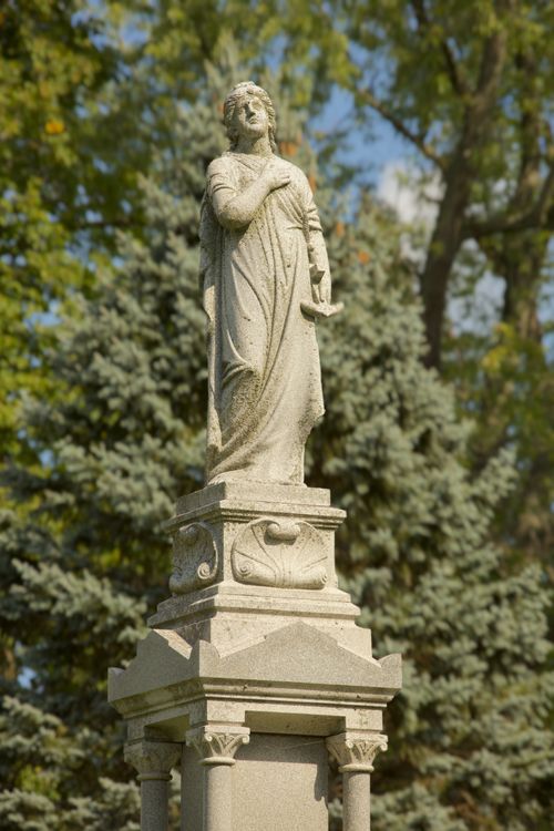 Free Vertical stone statue set against lush green trees in a serene park setting. Stock Photo