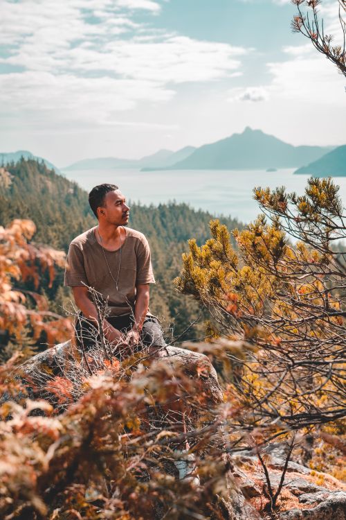 Free Man sits on rocky outcrop overlooking scenic Squamish landscape with mountains and forest. Stock Photo