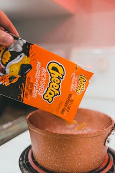 Cheetos mac and cheese being poured into a pot on an electric stove, highlighting casual cooking.