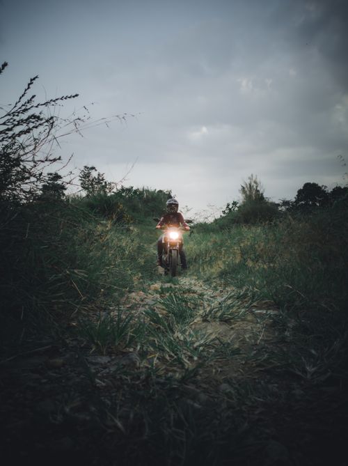 Free A person rides a motorcycle through a grassy field during dusk, creating a moody atmosphere. Stock Photo