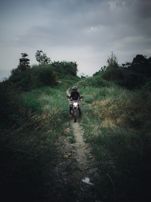 Free A motorcyclist on a rugged trail through lush highland terrain under a cloudy sky. Stock Photo