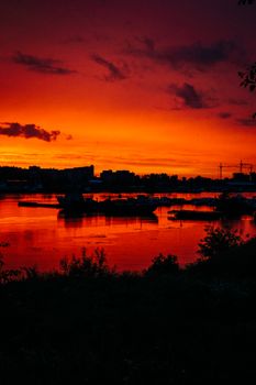 A breathtaking sunset over a calm body of water, with silhouettes of distant buildings and cranes.