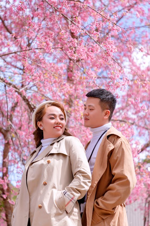 Man and Woman in Brown Coat Standing Near Pink Cherry Blossom Tree