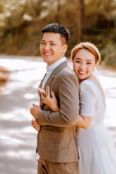 Joyful Asian bride and groom embracing outdoors on their wedding day.