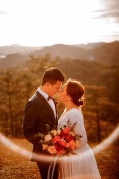 A bride and groom share an intimate moment outdoors during a sunset, holding a vibrant bouquet.