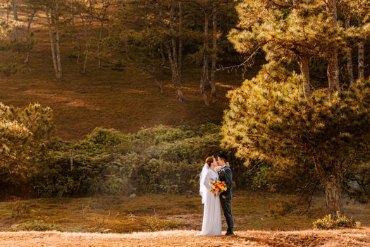 A couple kisses in a serene forest setting, embracing love on their wedding day.