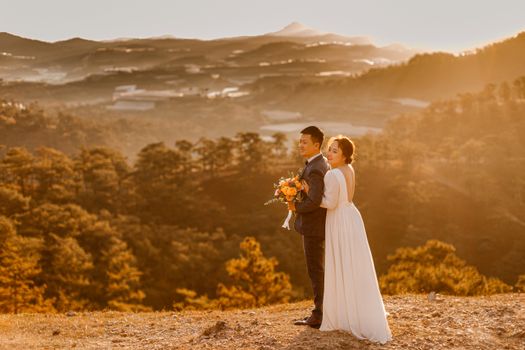 Asian couple embracing in an outdoor scenic wedding ceremony at sunset.