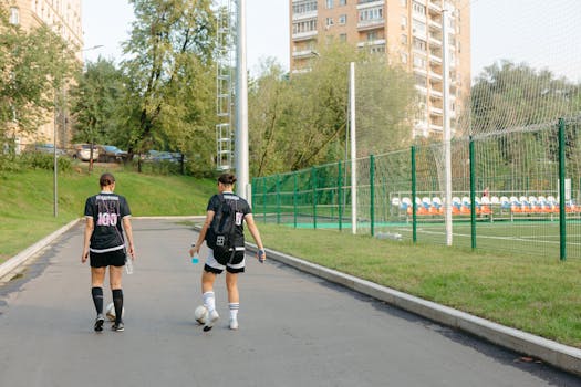 Two female soccer players walking near a field on a sunny day.