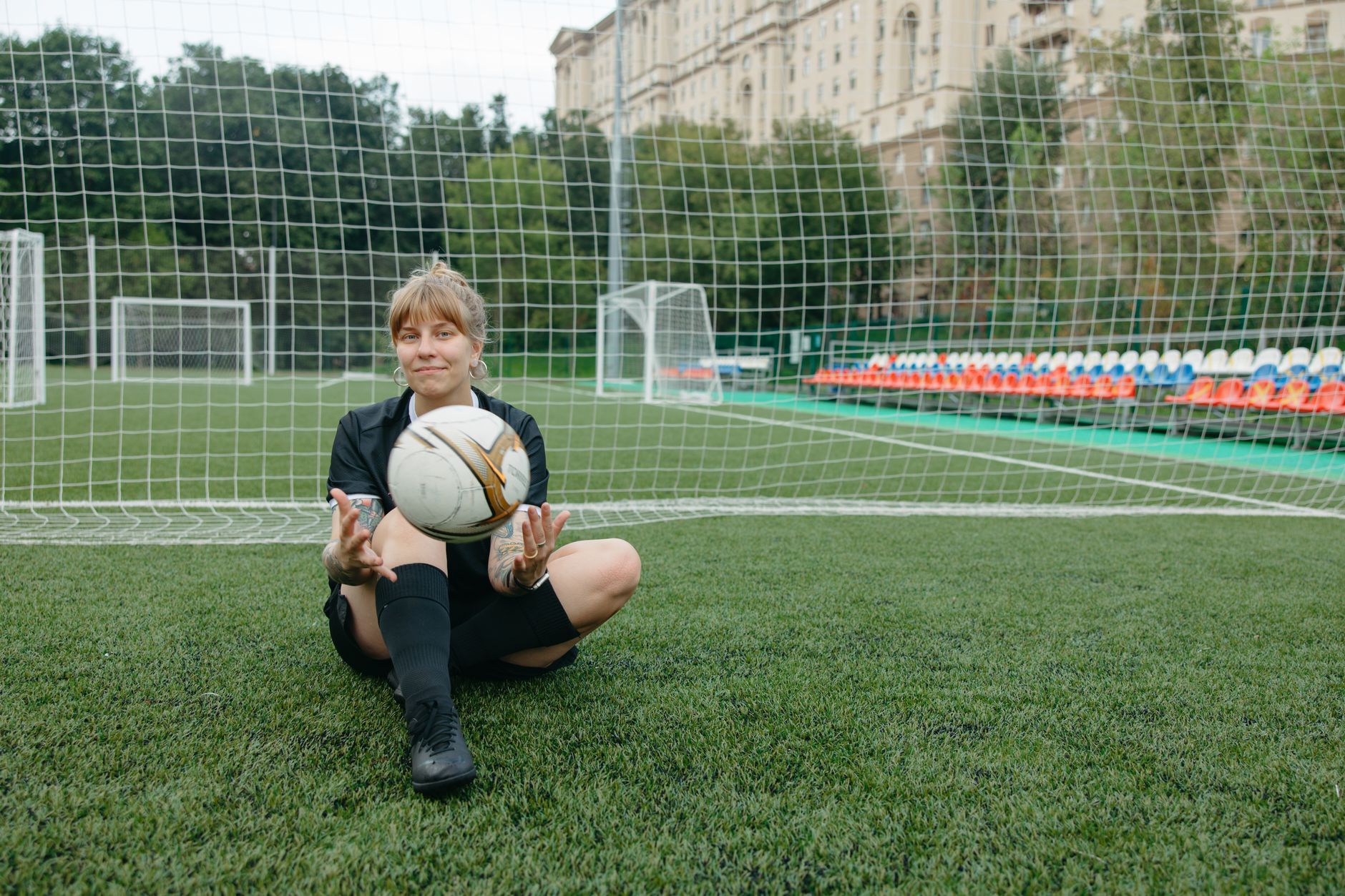 A female soccer player sitting with a ball on a soccer field, enjoying a break.
