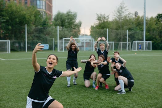 A women's soccer team takes a joyful group selfie on a soccer field, capturing the spirit of teamwork and fun.
