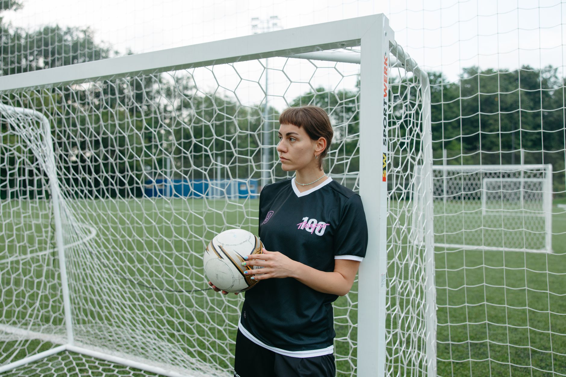 Jeune femme avec un maillot de football noir devant des cages de foot