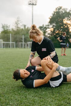 A female soccer player helps her injured teammate during a practice session on a soccer field.
