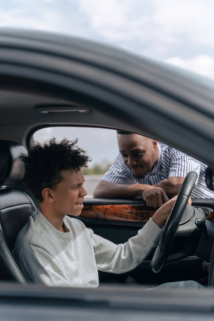 Adult Man Looking At A Teenager Seated On Driver's Side Of A Car 