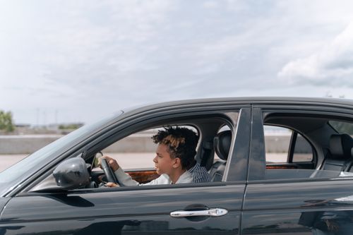 Free Side view of a young male teenager focused on driving a car in bright daylight. Stock Photo