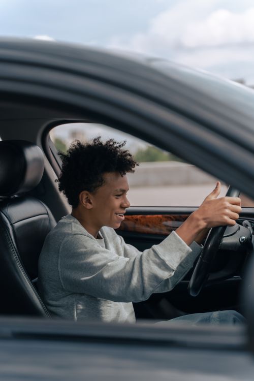 Free Teenager pretending to drive indoors, showing a happy expression while learning. Stock Photo