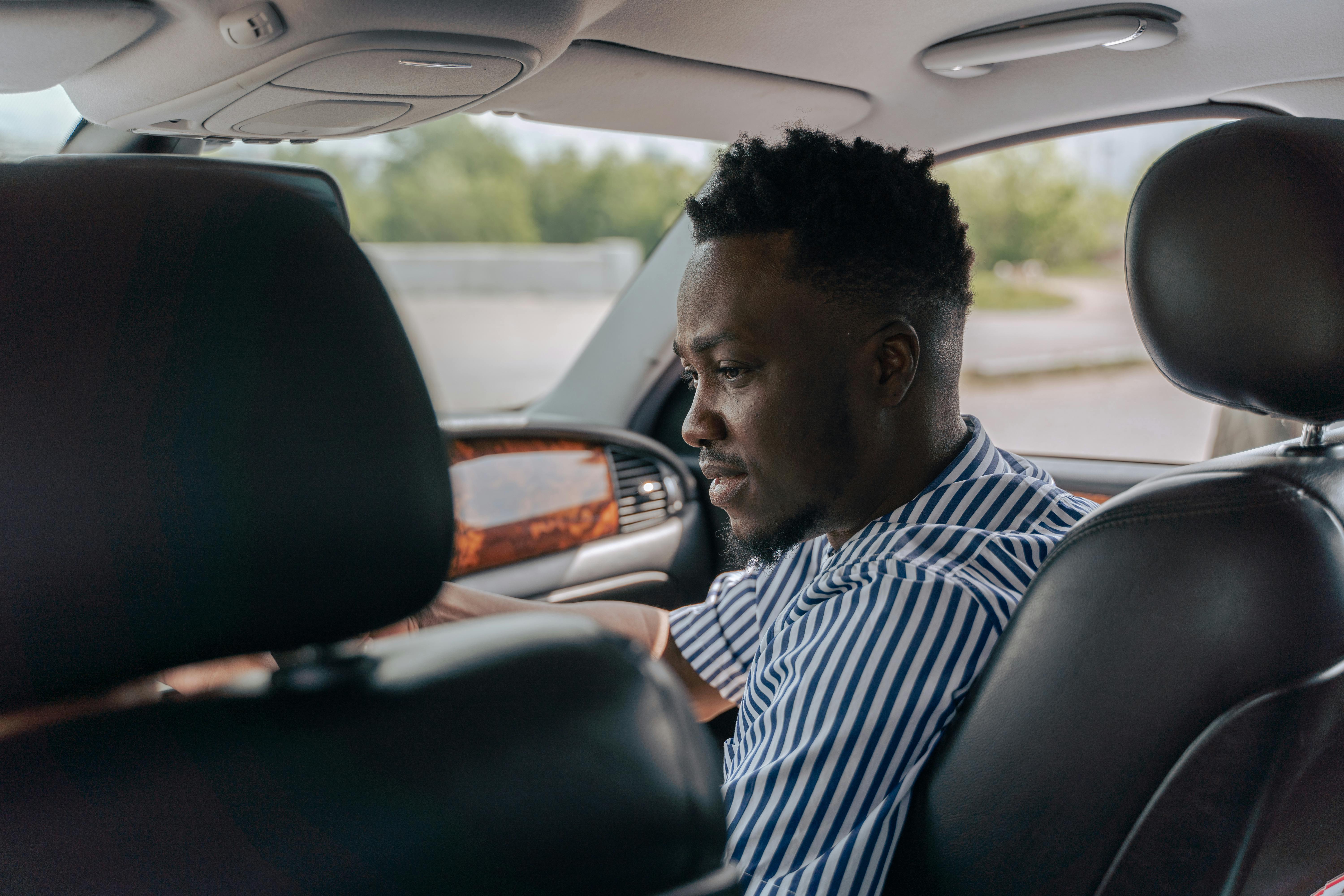 man in white and blue striped dress shirt driving car