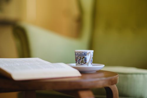 Free Close-up of a decorative coffee cup with an open book on a wooden table in a cozy indoor setting. Stock Photo