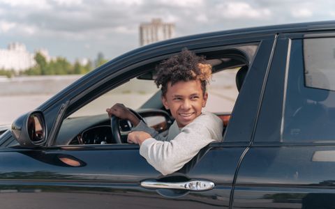 A smiling young driver sitting in a car on a sunny day