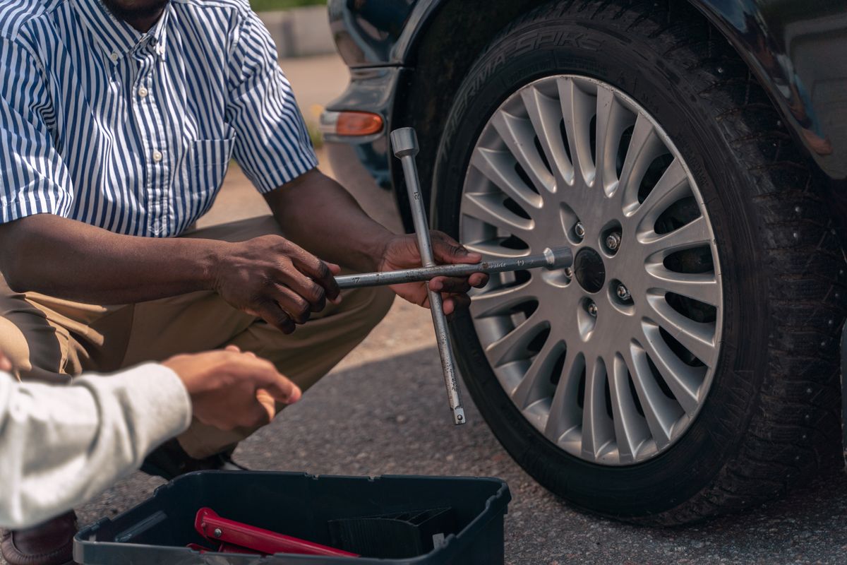 Adult demonstrating how to position a car jack and change a tire safely with tools on the ground