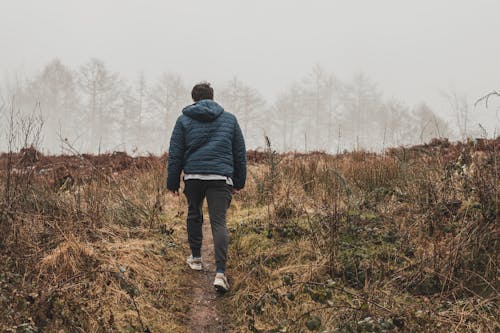 Man Wearing Blue Bubble Hoodie Jacket Walking on Green Grass Field