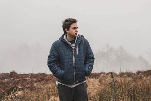 雾气弥漫的户外，一名穿着蓝色夹克的年轻人若有所思地站着