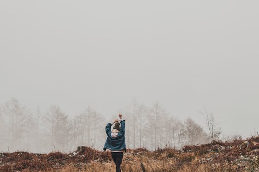 一名女子高举双臂，站在迷雾笼罩的森林里，四周雾气弥漫，树木环绕