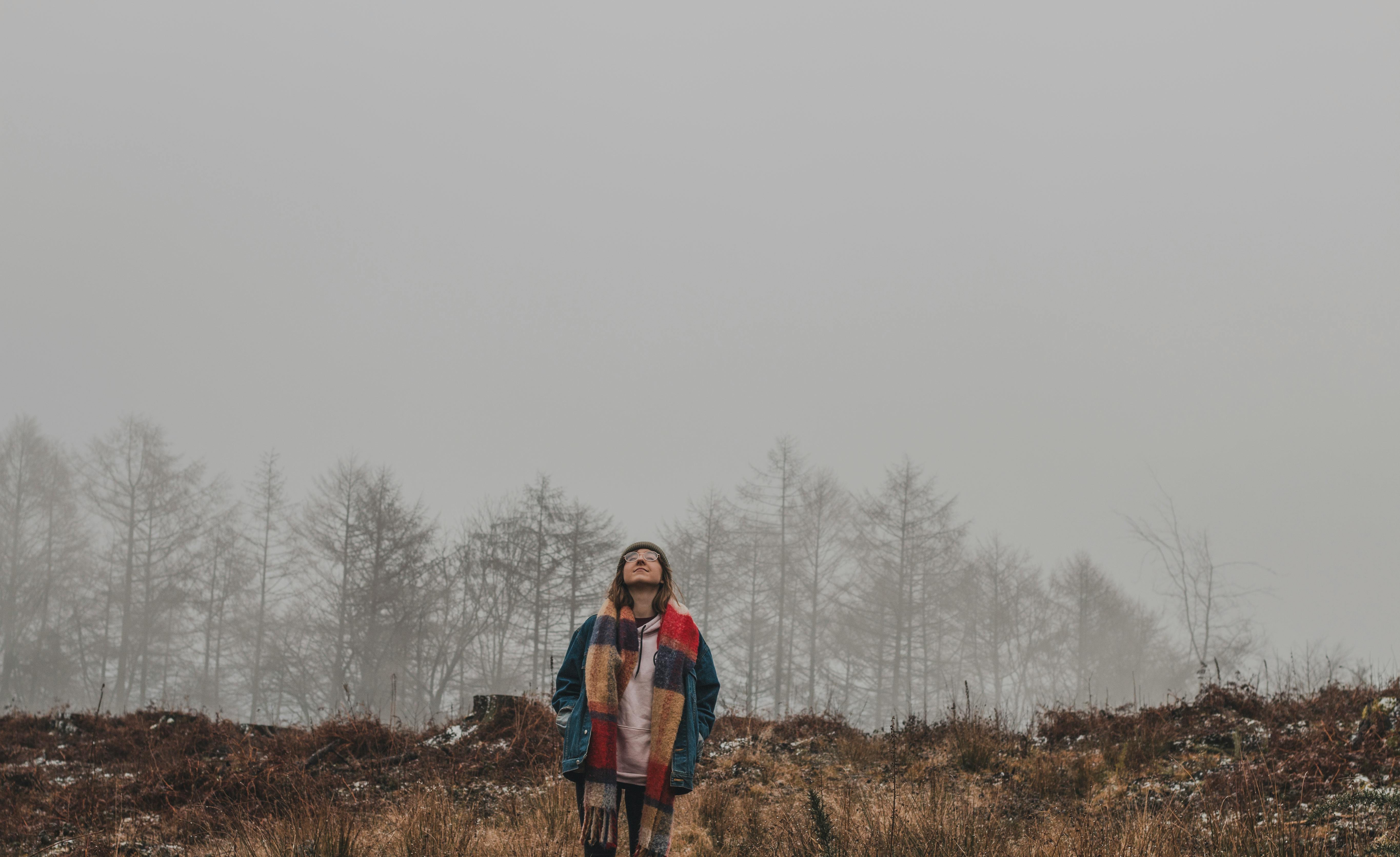 雾蒙蒙的森林里，一名女子独自站着，戴着彩色围巾