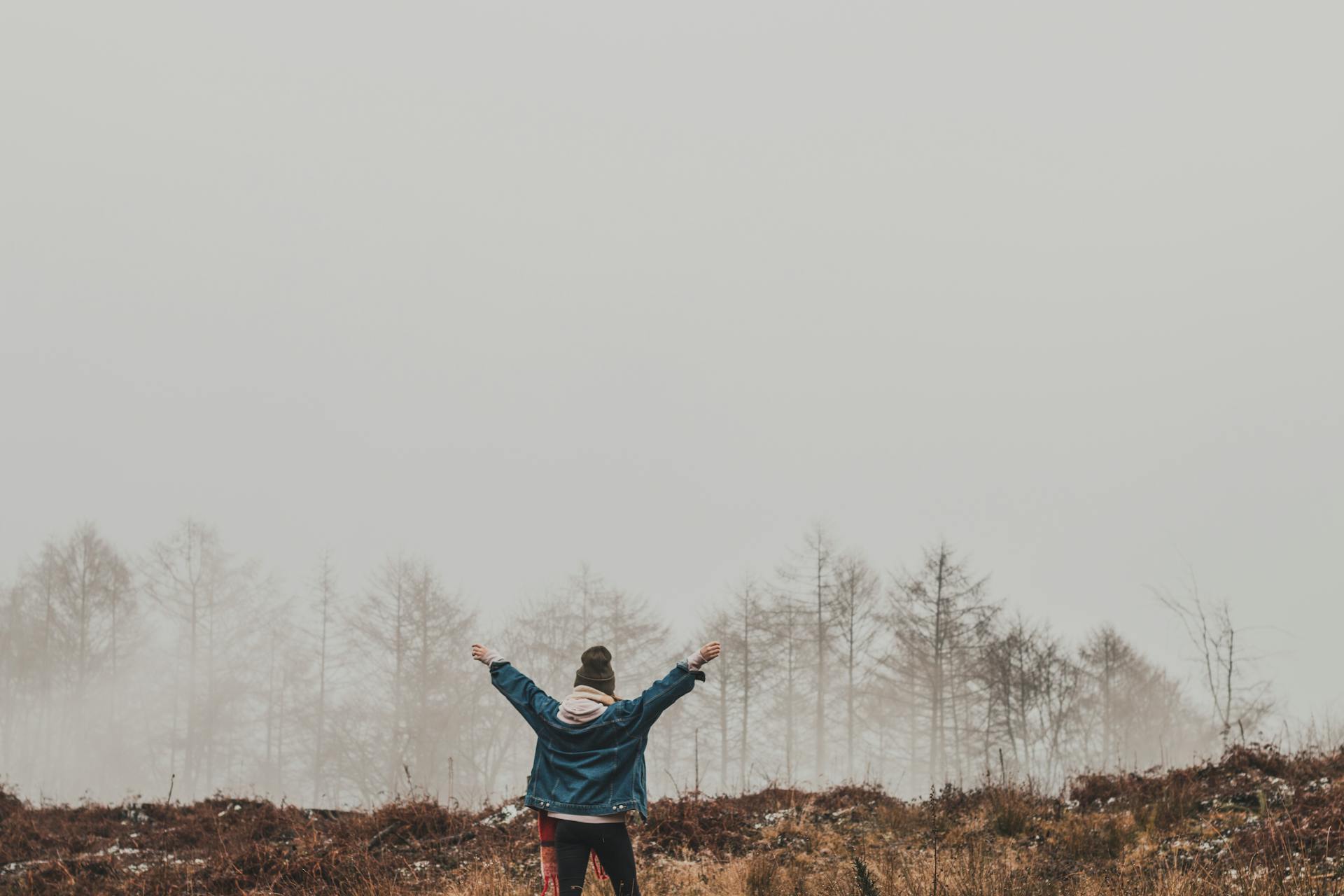 A person raises arms in a foggy forest landscape, embracing solitude and nature.