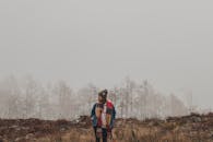 一名妇女裹着彩色围巾，走过雾蒙蒙的冬日景色，四周是霜冻的树木和贫瘠的土地