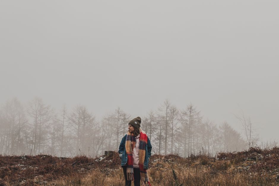 A woman bundled up in a colorful scarf walks through a foggy winter landscape, surrounded by frosty trees and barren ground.