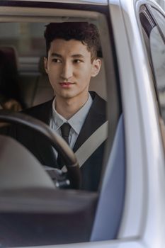Portrait of a young man in formal attire driving a car, looking away.