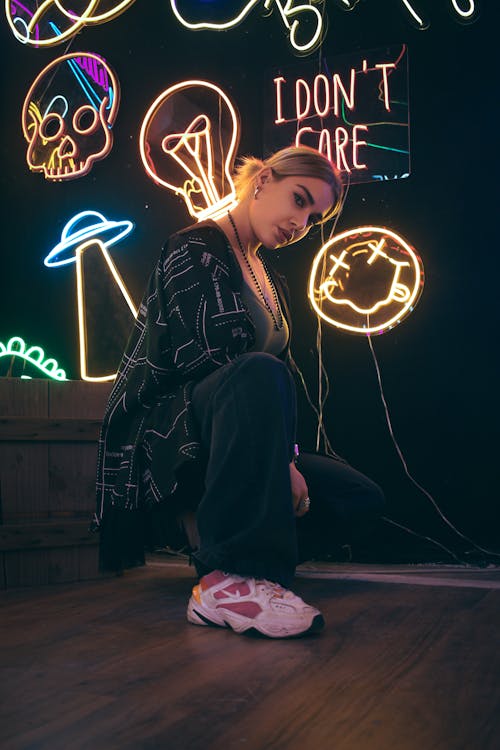 A Woman Sitting Beside a Wall with Neon Signages