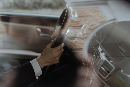 Close-up of a driver's hand on a luxury car steering wheel, shot inside the vehicle.