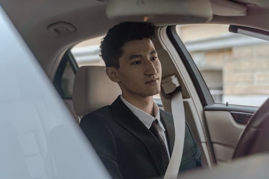 Young professional driver in formalwear inside a modern car, looking focused and attentive.