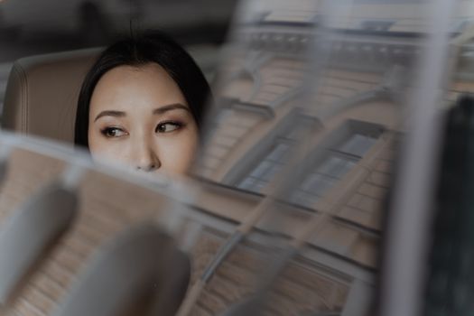 A thoughtful woman gazes out a car window reflecting building lines.
