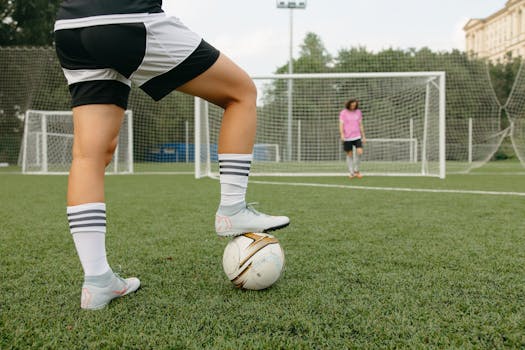 Two soccer players practicing on a field with goalposts in the background.
